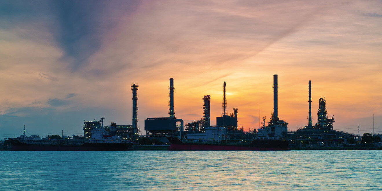 Raffinerie mit Meer im Vordergrund und Sonnenunaufgang im Hintergrund